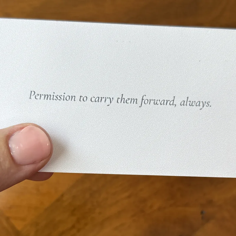 A hand holding a printed card that reads: Permission to carry them forward, always.